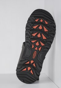 Black hiking shoe sole with aggressive tread patterns; features orange rubber accents and a textured surface for traction.