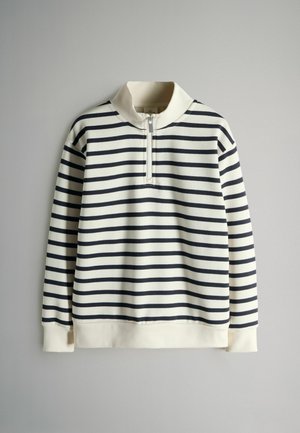 Randig tröja i krämfärg och marinblå, med halvdragkedja i kragen, ribbade ärmslut och en mjuk textur. Lodräta ränder skapar ett enhetligt mönster.