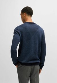 Maglione lavorato a maglia blu navy con un motivo testurizzato e polsini e orlo a coste solidi. La parte posteriore presenta disegni geometrici con texture di tessitura variabile.