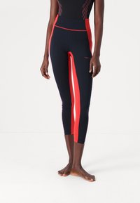 High-waisted leggings in navy with bold red side panels. Made from stretchy fabric. Features ankle-length design with a fitted silhouette.
