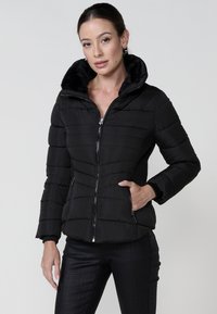 Chaqueta negra con cremallera, cuello de felpa, costuras horizontales, puños acanalados y bolsillos laterales. Presenta un diseño ajustado y una textura suave.