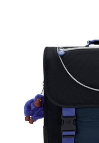 Mochila de tela negra con un acento azul, cierre de cremallera y un llavero de gorila morado desmontable. Cuenta con una solapa y una correa de hebilla en el frente.