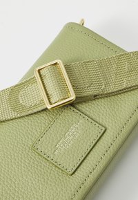 Roheline nahkministri kott tekstuuriga viimistlusega, millel on kuldne pandla ja põimitud rihm. Sisaldab ristkülikukujulist silti, millel on reljeefne tekst.