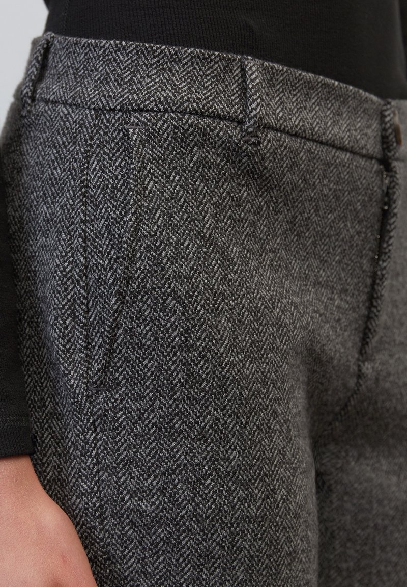 Pantalon gris à motif chevron en tissu texturé, doté de poches avant et d'une coupe classique avec un détail visible à la ceinture.