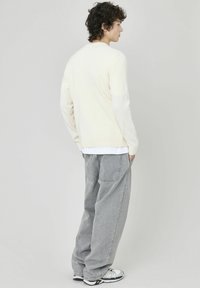 Pull en maille crème à manches longues, associé à un jean en denim gris ample. La tenue présente une coupe décontractée et des textures subtiles.