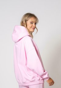 Rožinė oversized gobtuvė, su raišteliu, susiraukšlėmis juosmeniu ir rankovėmis. Minkšta medžiaga, lygi tekstūra ir laisvalaikio stilius.