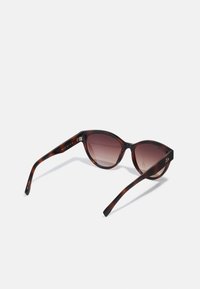 Sunglass s tigrí korytnačou so základným tvarom mačacích očí, s prechodovými hnedými sklami, elegantnými obrami a jemným logom na bočnej strane.