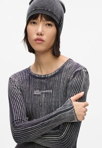 Top de manga larga y acanalado en gris oscuro con rayas verticales blancas. Presenta cuello redondo y logotipo "KARL LAGERFELD JEANS". El modelo lleva un gorro a juego.