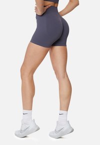 Vysoké športové šortky v tmavosivej látke s krátkym strihom. Obsahujú bezšvový dizajn a detail loga. Kombinované s bielymi športovými topánkami a ponožkami.