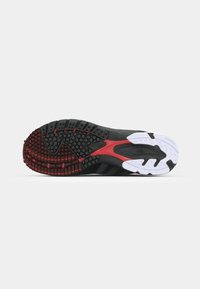 Black athletic shoe sole with a textured surface. Features red and white accents, multi-directional traction pattern, and rounded edges.