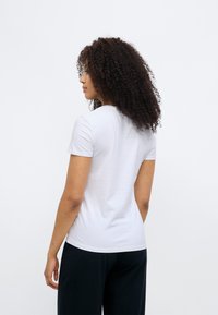 White cotton t-shirt with short sleeves, crew neck, and a fitted design, worn with black pants. Smooth texture, minimalistic style.