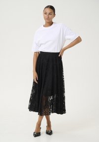 Gonna di pizzo nero con sovrapposizione trasparente e intricati motivi floreali, abbinata a una t-shirt bianca in cotone e décolleté nere a punta.