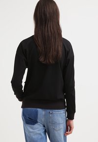 Felpa nera con vestibilità rilassata, polsini e orlo a costine, abbinata a jeans in denim blu chiaro con dettagli di patchwork.
