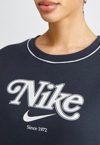 Marinblå sweatshirt med vit "Nike"-logotyp, rundad halsringning med vit kantning, mjuk tygstruktur, inga synliga mönster eller detaljer.