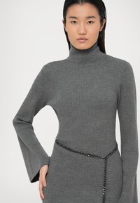 Grå, ribbet turtleneck kjole med lange, flagrende ærmer og et sort kædebælte, der har en tætsiddende silhuet og struktureret stof.
