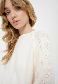 Maglione in maglia crema con maniche a motivi intricati e vestibilità rilassata. Tessuto morbido e scollo rotondo.