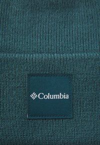 Gorro de malha em verde-água feito de tecido texturizado, com um emblema retangular da Columbia cosido na parte da frente.