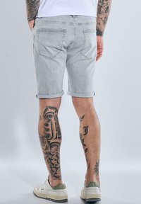 Light gray denim shorts with rolled hems, featuring back pockets and a smooth texture, paired with white and green sneakers.