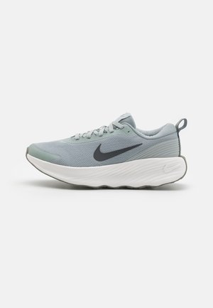 Zapatilla de running Nike gris claro con empeine de malla, logo Swoosh negro, suela blanca acolchada y lengüeta en el talón, vista lateral.