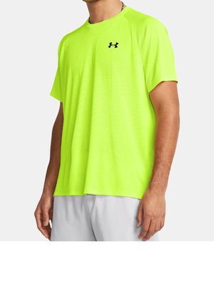 Man draagt een fel neon groen sportshirt met korte mouwen en een zwart Under Armour-logo op de borst en lichtgrijze shorts.