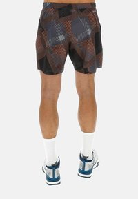 Jambes masculines portant un short à motifs noir, marron et gris, des chaussettes blanches, et des chaussures de sport blanches et bleues, vues de dos.