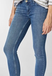 Skinny jeans in medium blue denim, featuring a classic five-pocket design, subtle whiskering, and a button closure.