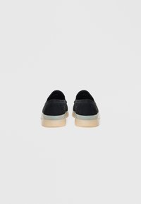 Sorte slip-on sko med en glatt skinnoverdel, lette gummier, avrundet form og minimalistisk design. Ingen synlige mønstre eller maskinvare.