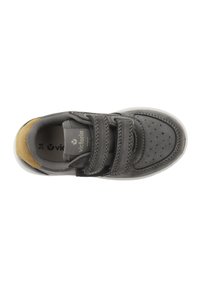 Zapatilla gris con un upper liso, correas de velcro, caja de puntera perforada y un acento en contraste en color marrón claro en el talón. Suela de goma blanca.