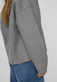 Grå fleece-tröja med avslappnad passform och sjunkna axelsömmar, parat med denimbla jeans. Mjuk struktur och minimala design detaljer.