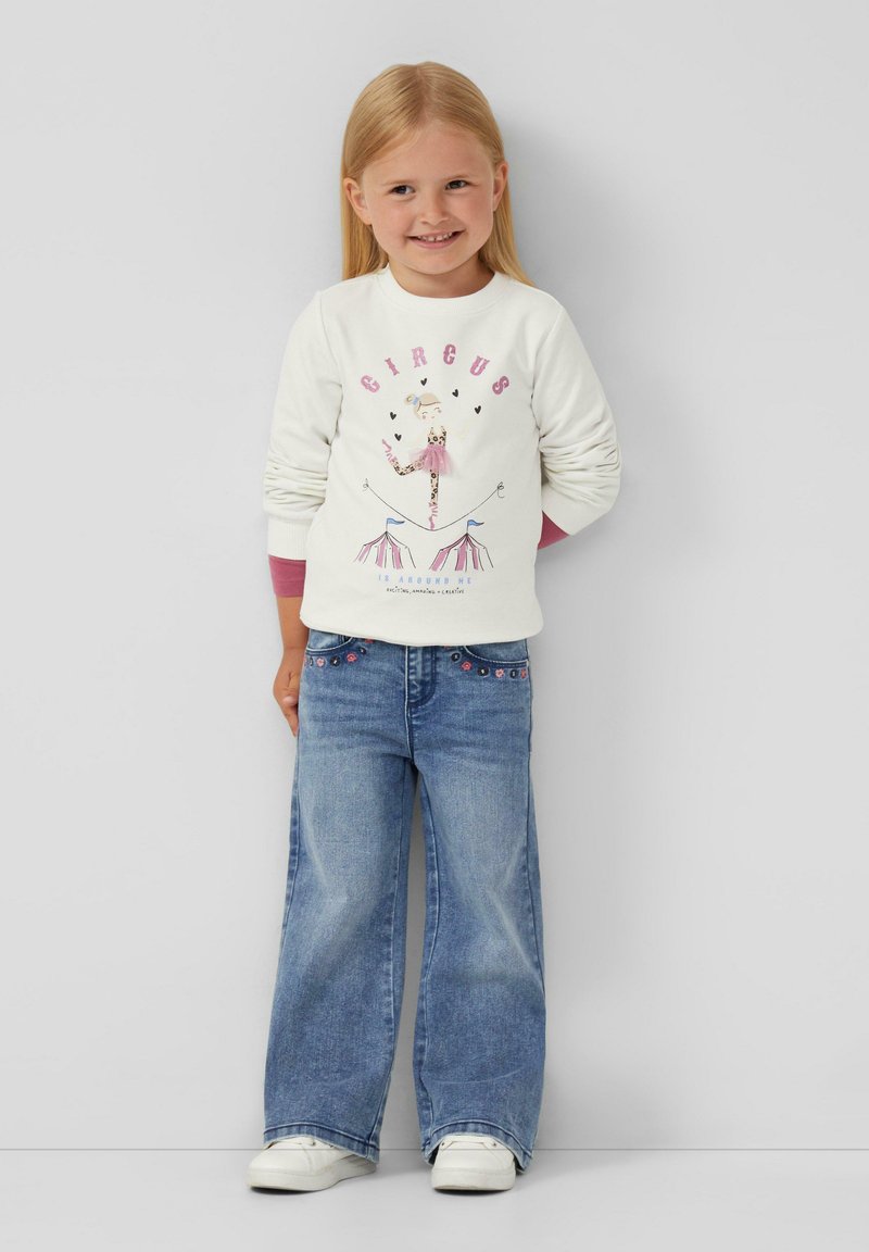 Biała bluza z nadrukiem "CIRCUS" oraz ilustracją tancerza; zestawiona z jasnoniebieskimi spodniami typu wide-leg z wyszywanymi detalami. Białe sneakersy.