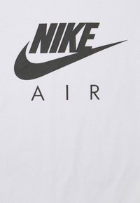 Bílý bavlněný tričko s výrazným černým logem Nike a slovem "AIR" pod ním, zobrazeným tučným bezpatkovým písmem.