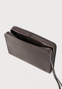 Σκούρο καφέ πορτοφόλι από δέρμα με υφή πέτρας, με δύο φερμουάρ και λουράκι καρπού, που φέρει διακριτικό λογότυπο Calvin Klein στο μπροστινό μέρος.