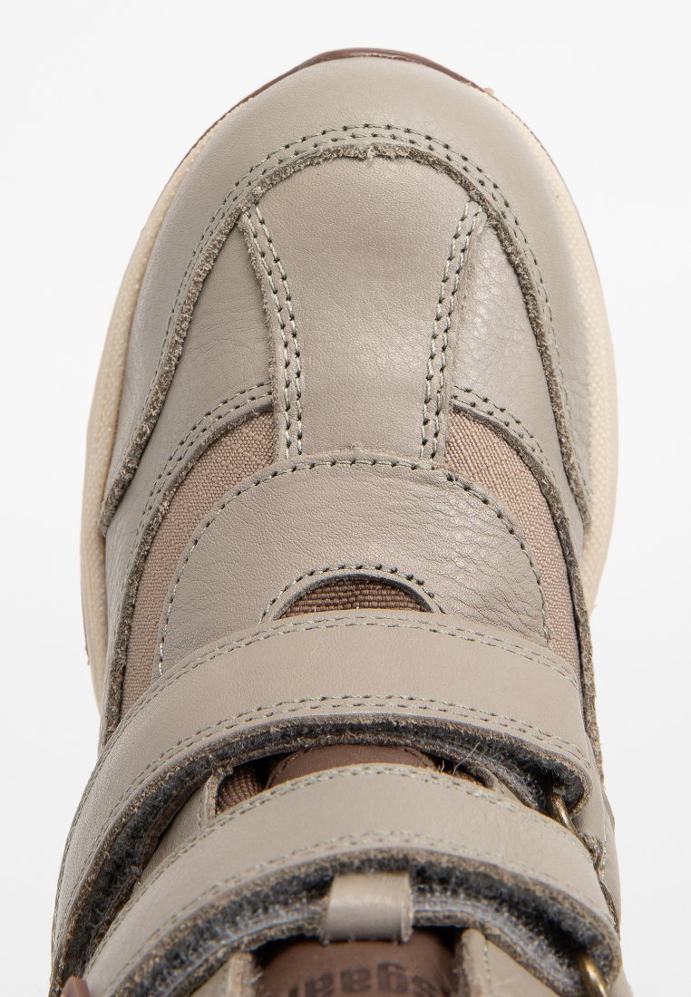 Grå lädersko med tre justerbara remmar, med en strukturerad yta och sydda detaljer. Rund tå och vadderad krage.