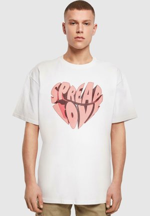 Fehér pamut póló, nagy szív grafikával, melyen a "SPREAD LOVE" felirat olvasható rózsaszín és piros árnyalatokban. Rövid ujjú és laza szabású.