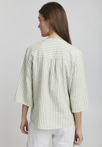 Top de lino a rayas en verde claro y blanco, con mangas tres cuartos, cuello redondo y un dobladillo ligeramente curvado. Tejido texturizado.