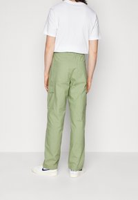 Ljust gröna cargobyxor av slitstarkt tyg med flera fickor, raka ben och avslappnad passform. Bärs med en vit t-shirt.