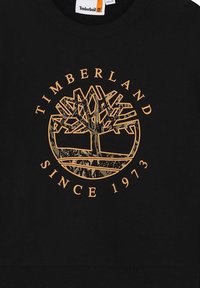 Felpa nera con logo di un albero dorato e la scritta "TIMBERLAND SINCE 1973" in un design a rilievo. Texture morbida, colletto a girocollo, stile casual.