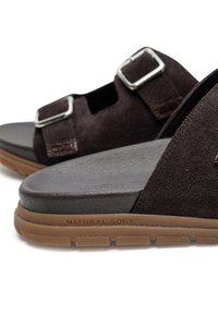 Brown suede sandals with two adjustable silver buckles, a black smooth insole, and a tan rubber outsole. "NATURAL SOFT™" branding visible.