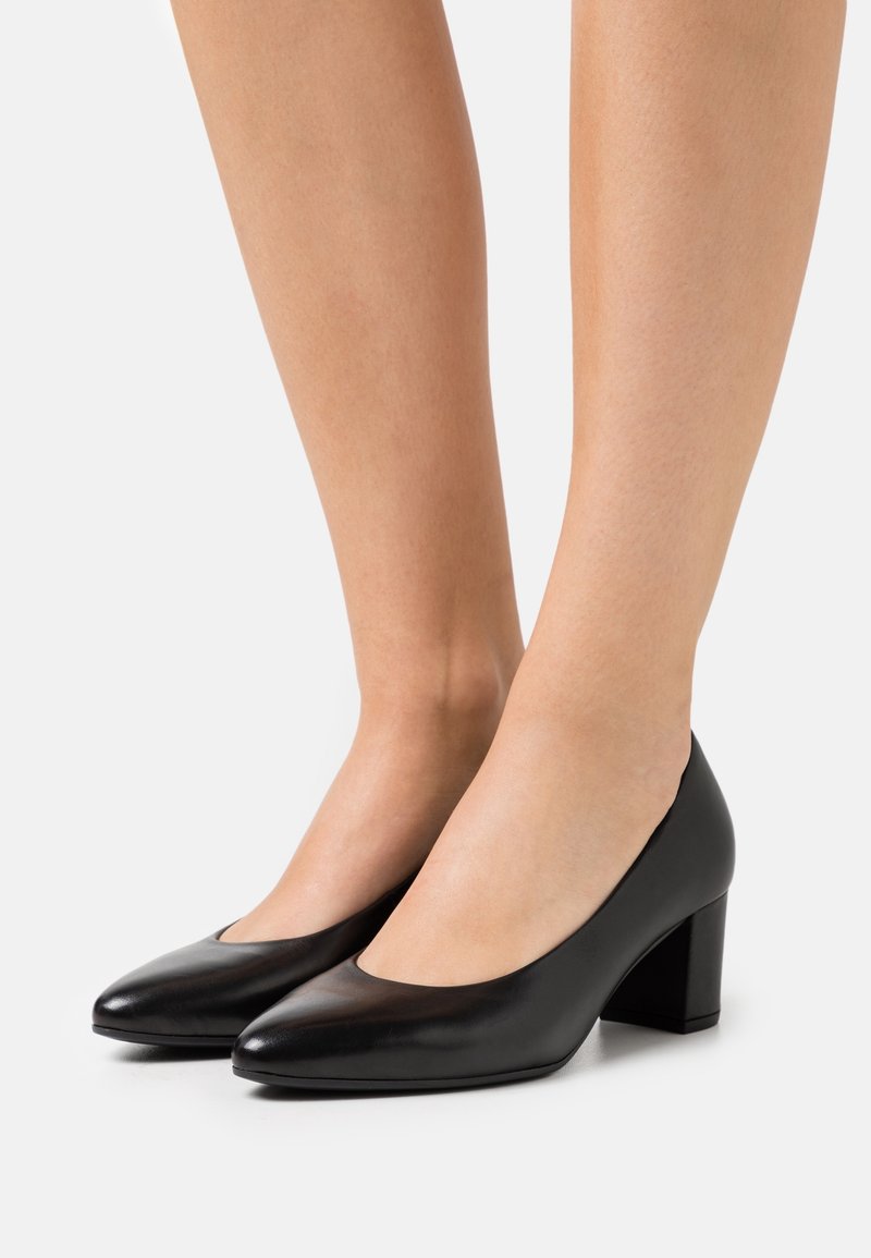 Chaussures à talons hauts en cuir noir avec un bout arrondi, un petit talon carré et une texture lisse. Design minimaliste et silhouette classique.