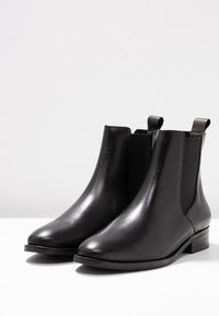 Botas Chelsea de cuero negro con textura suave, paneles laterales elásticos y lengüetas. Cuentan con un tacón bajo cuadrado y un diseño de punta puntiaguda.