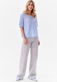 Lichtblauwe gebreide top met een gestructureerde open weving, gecombineerd met gestreepte wijde broek in tinten van wit en blauw.