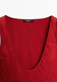 Haut sans manches rouge avec un décolleté en V profond, avec une étiquette noire visible à l'intérieur qui indique "Massimo Dutti, Fabriqué en Chine."
