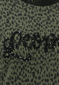 Gr�ünes gemustertes Strickoberteil mit schwarzem Pailletten-Textverzierung und einem strukturierten, gerippten Halsausschnitt.