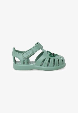 Sandalia verde para niño pequeño con tiras cerradas en la punta, correa ajustable de velcro en el tobillo y una pequeña decoración de rana en la parte superior.