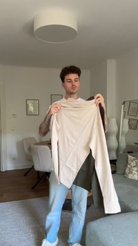 Dugih rukava u bež i maslinastoj boji, s jedinstvenim asimetričnim dizajnom, izrađena od glatkog, rastezljivog materijala. Drži je osoba unutra.