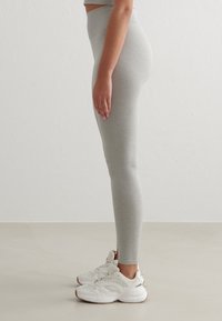 Šedé legíny s vysokým pasem vyrobené z měkké, elastické tkaniny, doplněné bílými sportovními botami s texturovanými akcenty a zakřiveným designem.