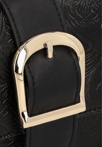 Cintura in pelle nera con motivo floreale in rilievo, dotata di una fibbia rettangolare dorata con chiusura a perno. Design texturizzato e dettagliato.