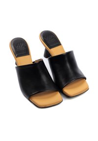 Mule nere in pelle aperte all'aperto presentano una fascia larga e un tacco a blocco color tan. La soletta è anch'essa tan, con un marchio impresso sul tacco.