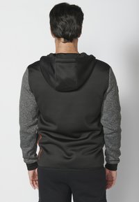 Sudadera negra con mangas texturizadas grises, que cuenta con una capucha con cordón y un acabado suave. Incluye un detalle de logo y puños acanalados.