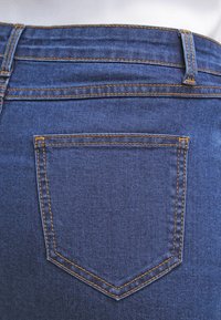 Mörkblå denimjeans med kontrasterande gul sömnad, med en liten rektangulär bakficka och en rak midjedesign.